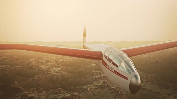 The white sailplane calmly gliding in the sky over the snow-covered mountains. alt