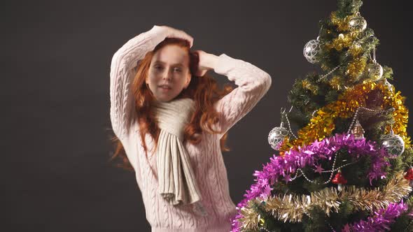 Portrait of Happy Redhead Girl Dancing Near Christmas Tree in Studio on Black Background alt