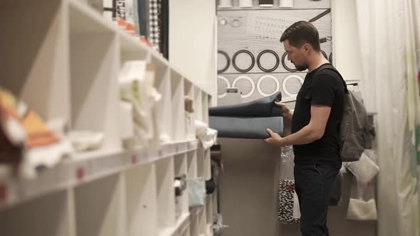 Young Man is Examining Fabric in a Drapery Store Taking Rolls From Shelfs alt