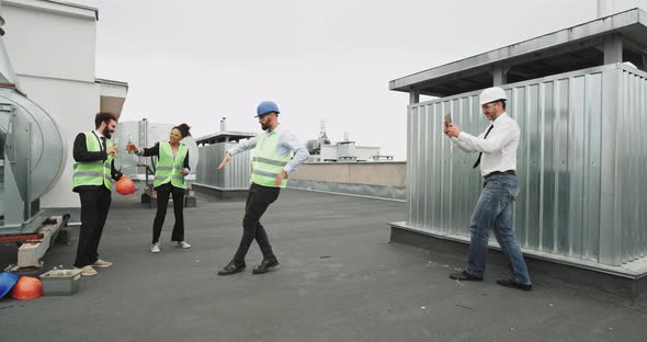 A Young Handsome Man Dances While Two Other Worker alt