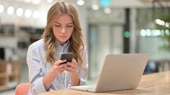 Businesswoman with Laptop Using Smartphone in Office  alt