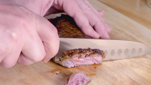 Slow Motion Shot of Slicing a Medium Rare Ribeye Steak on a Wooden Cutting Board alt
