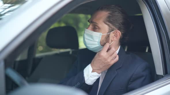 Young Caucasian Man Closing Car Door Taking Off Coronavirus Face Mask Sighing alt