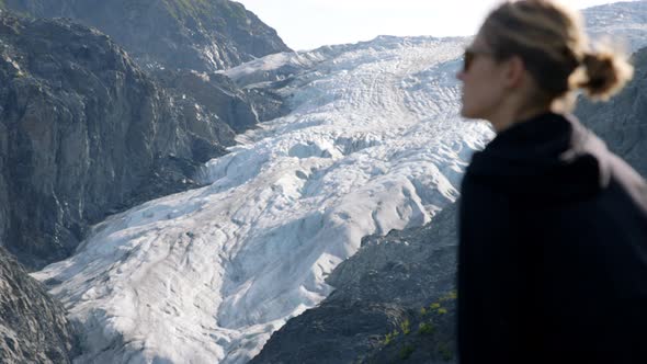 Female Standing in Front of Alaskan Glacier, Slow Motion Changing Depth of Focus Shot. Global Warmin alt
