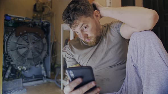 A Man Fixes a Washing Machine and Watches Instructions on His Phone