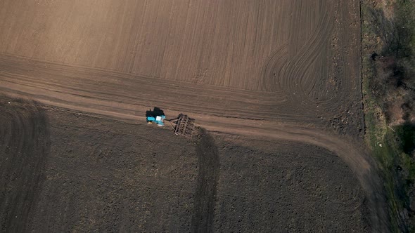 Top View of a Tractor with Harrow System Plowing Ground on Cultivated Farm Field alt