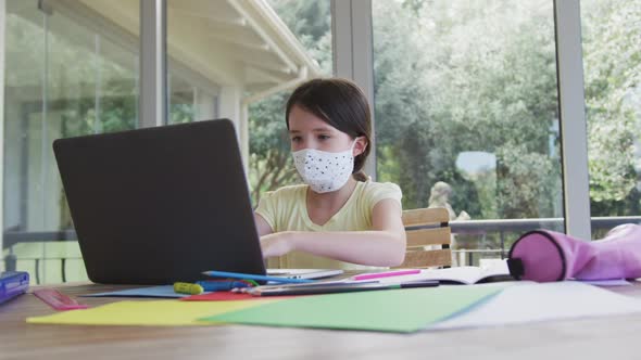 Girl wearing face mask using laptop at home alt