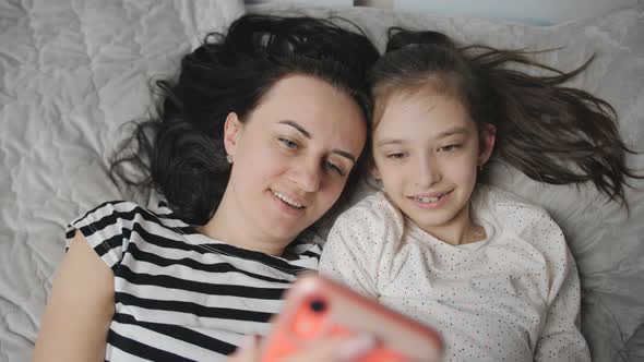 Happy Caucasian Woman Enjoying Family Time with Daughter Lying on Bed Smiling Taking Selfies with