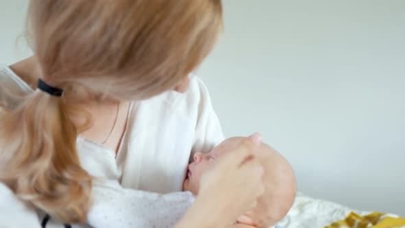 woman stroking and kissing a sleeping baby in her arms