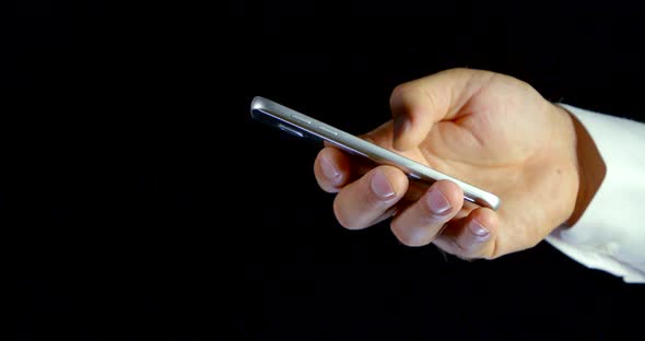 Close-up on a Black Background a Man's Hand with a Mobile Phone Access To the Internet alt