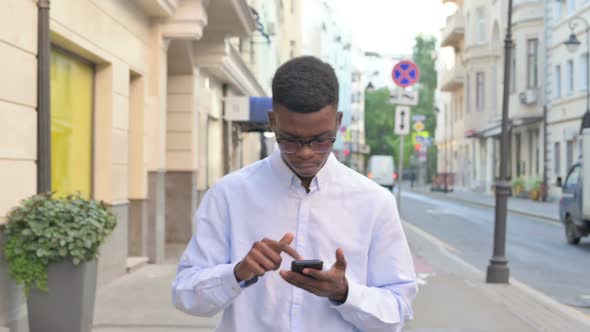 African Man Using Smartphone While Walking on the Street alt