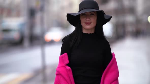 a Brunette in a Black Hat and a Bright Pink Coat Taken Off Shoulders Walks Against the Background of alt
