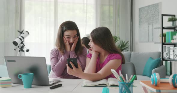 Cute happy girls doing their homework, they are connecting online and getting distracted