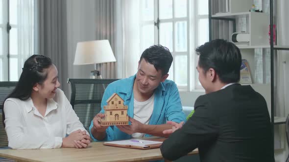 Asian Couple With A House Purchase Contract Paper Receives The House Model From A Real Estate Agent alt