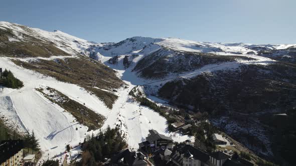 Flyover Sierra Nevada town towards Snowy mountain with ski resort tracks, Andalusia