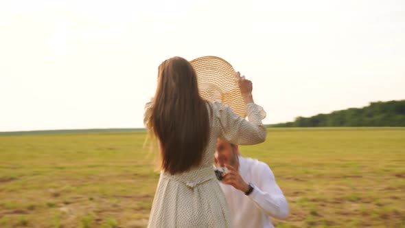 A Man Photographs a Woman in a Straw Hat on a Film Camera in a Field at Sunset
