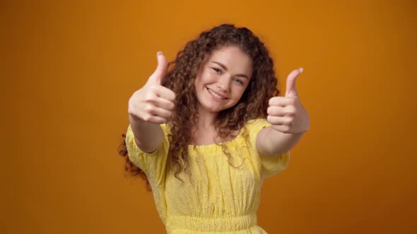 Young Curly Haired Woman Showing Thumbs Up Sign Against Yellow Background