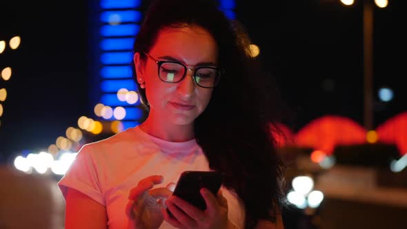 Pretty Woman Stands on the Street in a White T-shirt and Glasses, Makes Online Payments By Credit alt