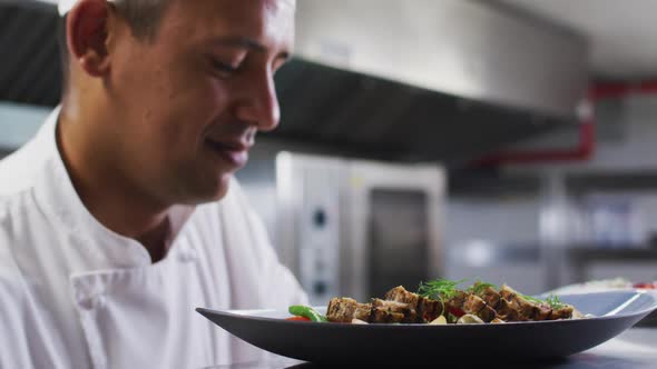 Caucasian male chef garnishing dish and smiling in restaurant kitchen alt