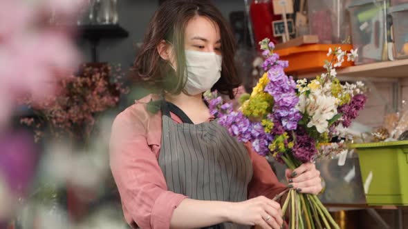 Woman in Facial Protective Mask Finishing Completing Bouquet. Asian Female Florist Arranging