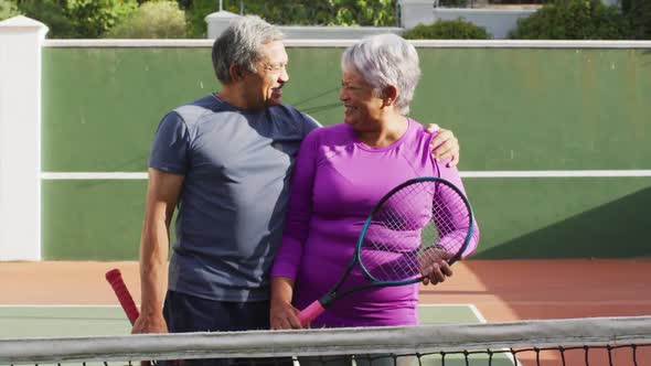 Video of happy biracial senior couple holding rackets on tennis court alt