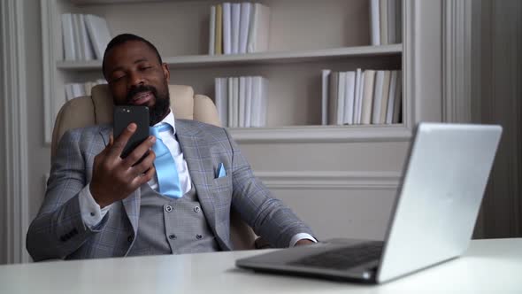 African-American Sleepy Bearded Man in a Gray Suit and Shirt. The Businessman Is in a Bright Office alt
