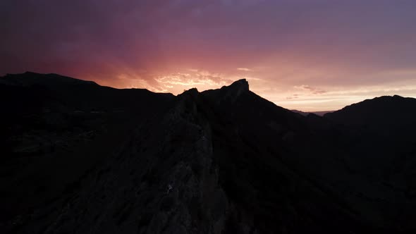 Colorful sky contrasting with black rock silhouette alt