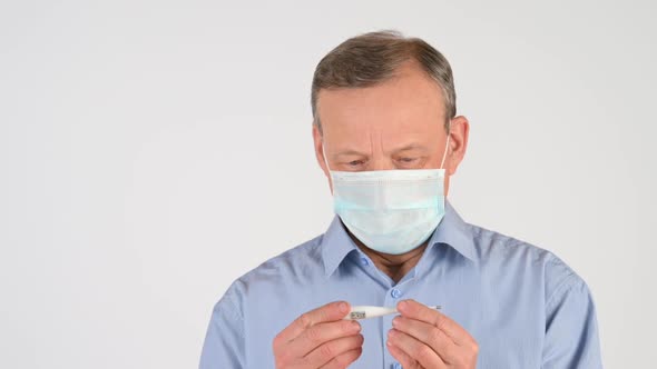 man in a medical mask measures the temperature with a thermometer
