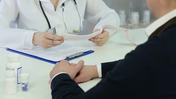 Female cardiologist checking patient's cardiogram, filling in medical history alt