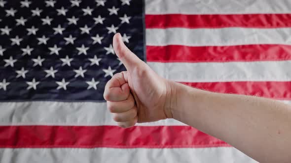 Thumbs Up and Thumbs Down Gestures Made with Caucasian Hand in Front of Blurry US Flag