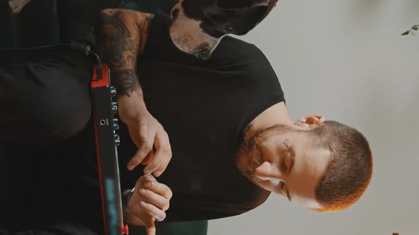 Vertical Video Young Bearded Musician Creates Music on MIDI Controller Keyboard and Amstaff Dog Sits alt