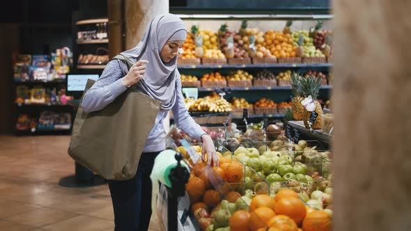 Portrait of Young Muslim Woman in Hijab Choosing Fruits in the Supermarket alt