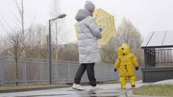 Mother with Small Cute Child in Yellow Waterproof Rain Pants Raincoat and Rubber Boots for Kids alt