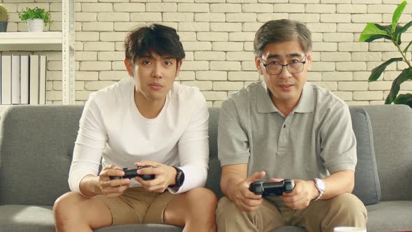 Asian father and son happily enjoy video games at home on vacation alt