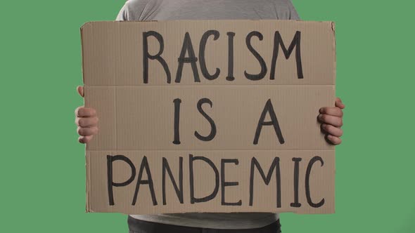 A Man Holds in Front of Him a Poster From a Cardboard Box with the Words RACISM IS A PANDEMIC alt
