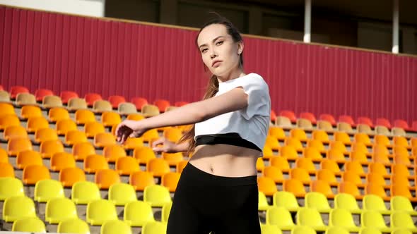 Young Female in Sportswear Stretching Body on Background of Sports Stadium alt