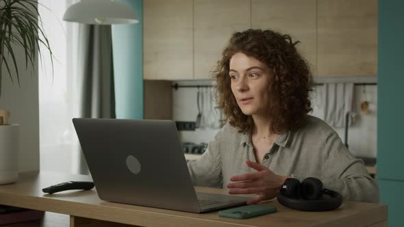 Curly 20s Caucasian Woman Greeting and Talking with Her Friends on a Video Call in Her Apartment alt