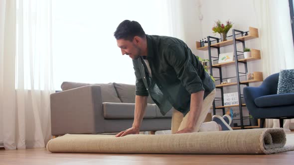 Happy Smiling Young Man Unfolding Carpet at Home alt