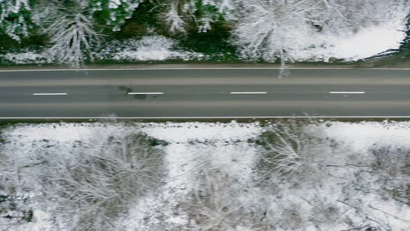 Empty street in a snow covered forest, flying straight from right to left by drone in a top down vie alt