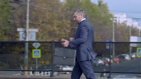 Businessman drinking coffee and using smartphone on foot