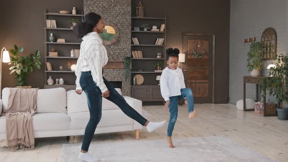 Active African Mom Babysitter American Energetic Little Kid Daughter Jumping Dancing in House Living alt