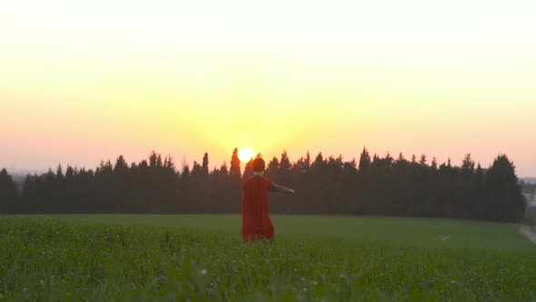 Boy dressed with a Superman cape running in a field, looking into the sunset alt