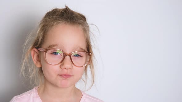 Little Girl in Glasses and a Pink Tshirt Indulges Has Fun and Shows Her Tongue Making Faces at the alt