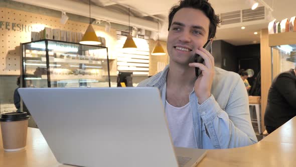 Young Man Talking on Mobile Phone Sitting in Cafe alt