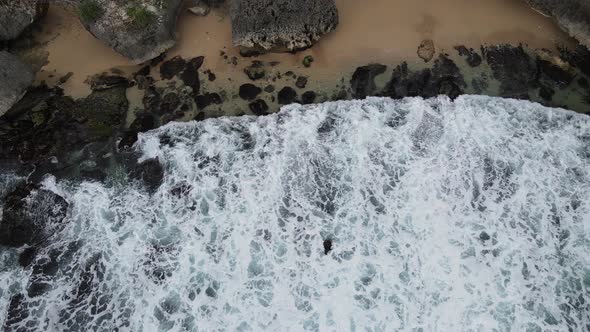 Top down aerial view of giant ocean waves crashing and foaming in coral beach alt