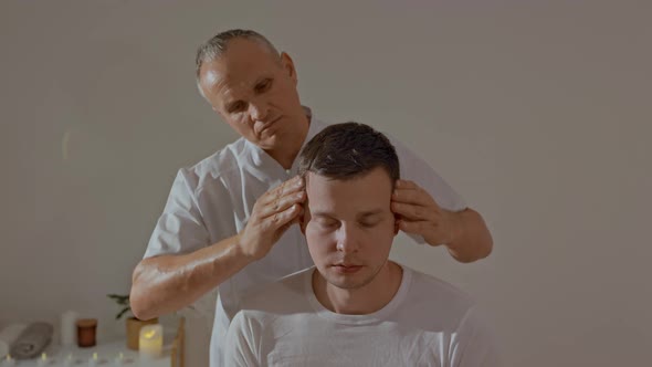 Young Man Relaxing During Professional Head Massage in SPA Salon