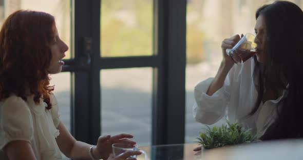 Two young women talking to each other while having a coffee break at work. Slow motion, medium shot. alt