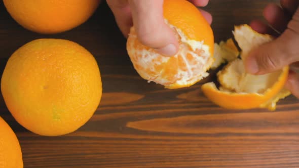 Male hand peeling orange citrus fruit on wooden background, top view