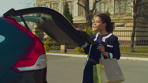 Happy Woman with Shopping Bags Near Car Trunk alt