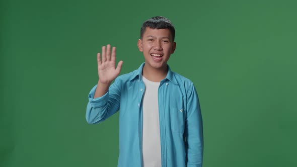The happy young Asian man waving hand while standing on green screen in the studio alt